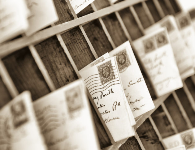 old fashioned letters and postcards sorted into old fashioned wooden mail box slots. 1930s postmarked British stamp at frame centre.